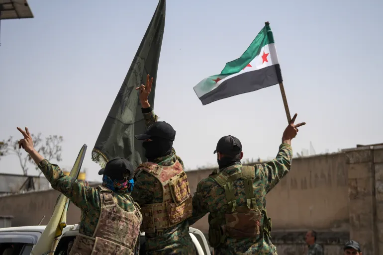 Members of the Syrian Democratic Forces (SDF) flash the victory sign while departing the city of Aleppo, Syria.